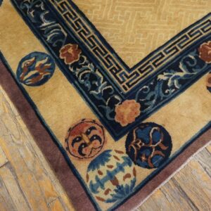 Gold rug with dark blue borders, colorful round motifs, and a patterned field lies on distressed wood planks.