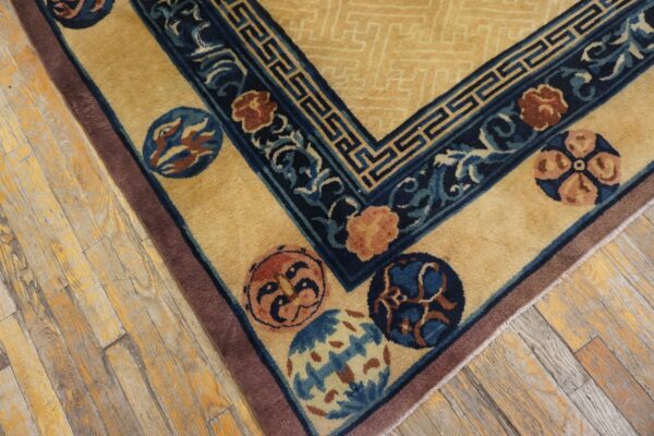 Gold rug with dark blue borders, colorful round motifs, and a patterned field lies on distressed wood planks.
