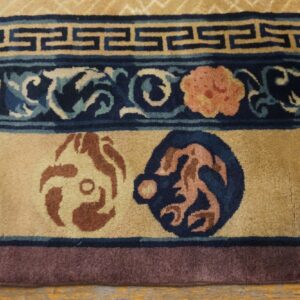 Tan high-pile rug detail displays dark blue borders with fretwork, floral designs, and rust circular motifs on wood flooring.