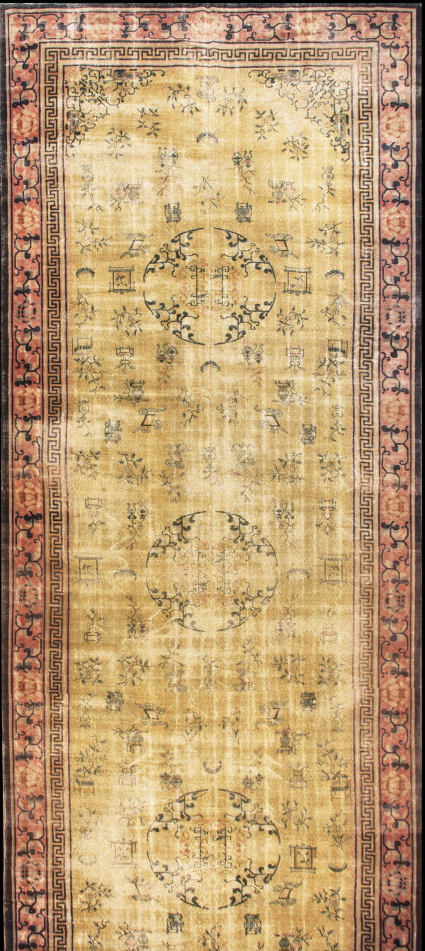 A distressed gold runner rug displays dark symbolic patterns and medallions, framed by pink and black borders.