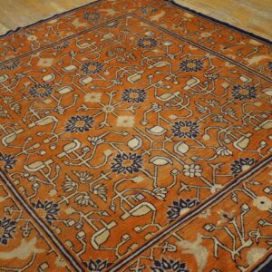 Traditional orange rug with a detailed navy and tan floral pattern resting on light hardwood planks.