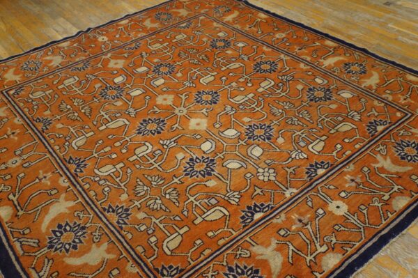 Traditional orange rug with a detailed navy and tan floral pattern resting on light hardwood planks.
