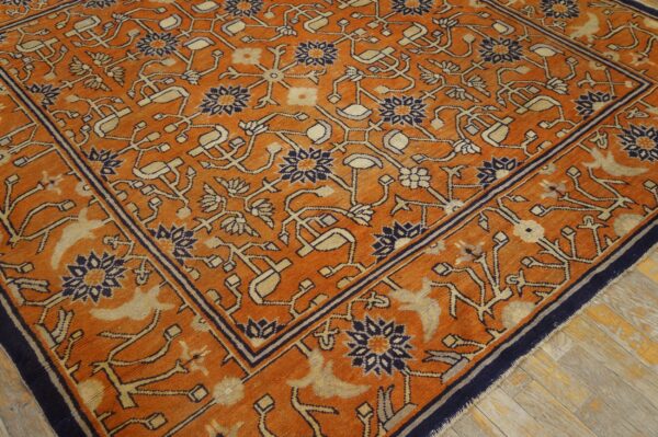 Angled view of an orange rug featuring intricate navy and tan botanical designs over rustic wood planks.