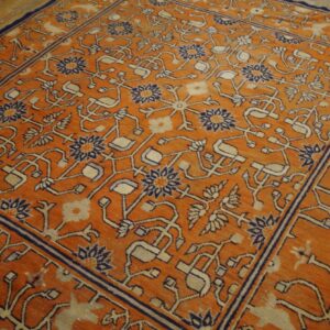 Orange rug with intricate navy and cream stylized patterns covers wooden plank flooring.
