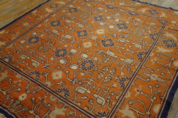 Orange rug with intricate navy and cream stylized patterns covers wooden plank flooring.