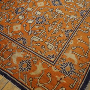 Burnt orange rug featuring complex beige and navy geometric and animal patterns, placed on light hardwood floors.
