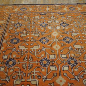 Bright orange rug with complex stylized floral patterns in navy blue and cream on a wooden floor.