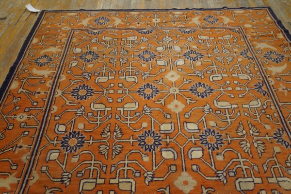 Bright orange rug with complex stylized floral patterns in navy blue and cream on a wooden floor.