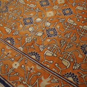 Low-pile orange rug with traditional navy and tan vine and floral patterns over distressed wood floor.