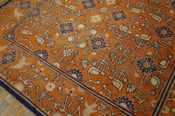 Low-pile orange rug with traditional navy and tan vine and floral patterns over distressed wood floor.