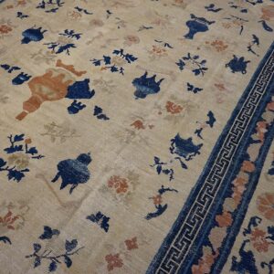 Scattered blue and rust botanical pattern on a distressed beige rug with a detailed blue key border.
