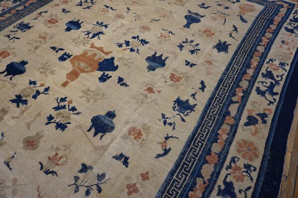 Scattered blue and rust botanical pattern on a distressed beige rug with a detailed blue key border.