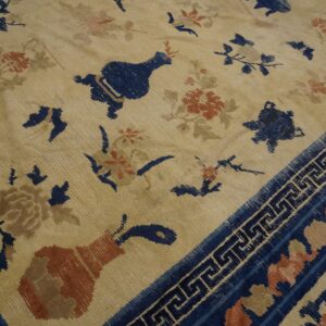 Low-pile beige rug with scattered blue and rust floral motifs and a dark blue geometric border.