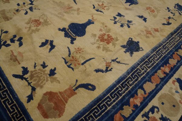 Low-pile beige rug with scattered blue and rust floral motifs and a dark blue geometric border.
