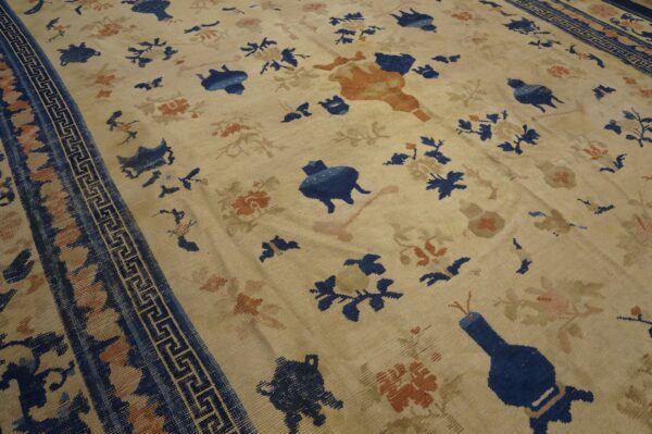 Cream rug with scattered dark blue and rust stylized motifs and a blue greek key border.