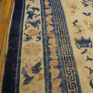 Low-pile rug featuring blue and coral floral patterns and a meander border stripe on distressed wooden floorboards.