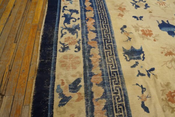 Low-pile rug featuring blue and coral floral patterns and a meander border stripe on distressed wooden floorboards.