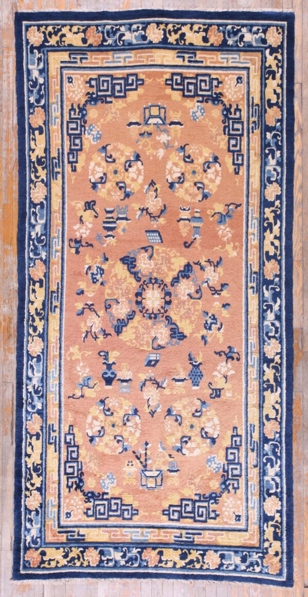 Coral rug featuring navy, light blue, and gold geometric and floral patterns, displayed on wood plank flooring.
