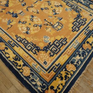A close-up of an orange rug featuring navy blue and yellow floral borders on rustic wooden plank floors.