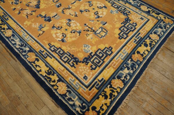 A close-up of an orange rug featuring navy blue and yellow floral borders on rustic wooden plank floors.