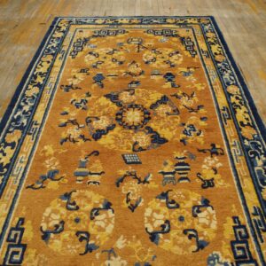 Mustard and navy patterned rug featuring floral and geometric motifs lying on yellow distressed hardwood.