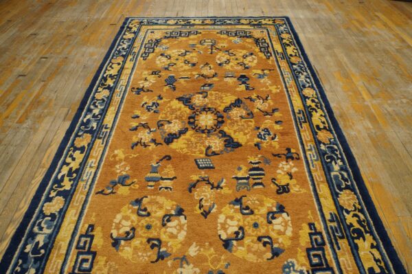 Mustard and navy patterned rug featuring floral and geometric motifs lying on yellow distressed hardwood.