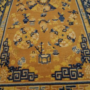 Traditional tan and navy rug featuring detailed floral motifs and geometric borders on distressed wood flooring.