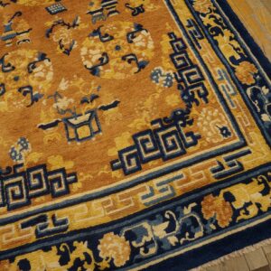 Thick-piled, orange, navy blue, and yellow patterned rug bordered with fret motifs rests on wood flooring.