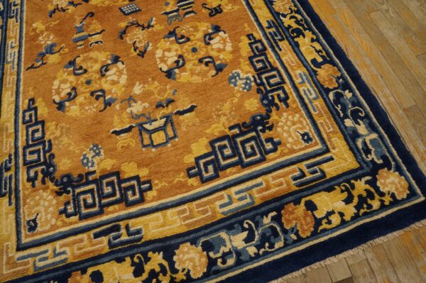 Thick-piled, orange, navy blue, and yellow patterned rug bordered with fret motifs rests on wood flooring.