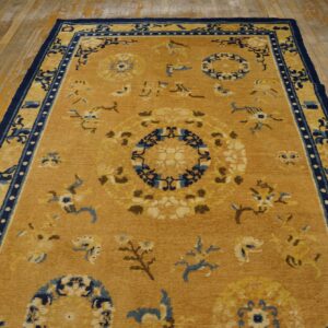 Mustardy yellow rug featuring blue and cream floral motifs and a wide navy border on distressed wood floor.