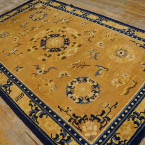 Mustard yellow rug with dark blue floral medallions and borders rests on worn wood flooring.