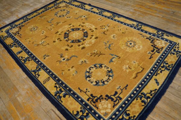 Mustard yellow rug with dark blue floral medallions and borders rests on worn wood flooring.