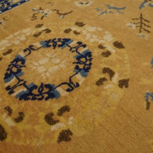 Textured golden-tan rug detail showing a navy blue medallion and scattered cream and brown botanical patterns.