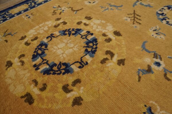 Textured golden-tan rug detail showing a navy blue medallion and scattered cream and brown botanical patterns.