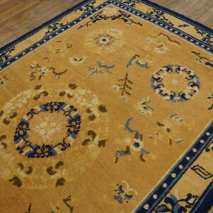 Traditional gold rug featuring navy blue and cream floral designs sits on distressed plank wood floors.