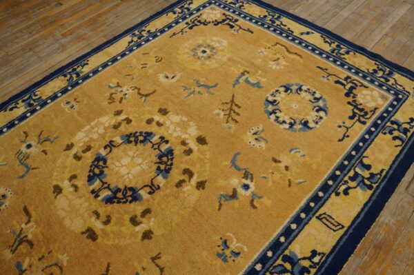 Traditional gold rug featuring navy blue and cream floral designs sits on distressed plank wood floors.
