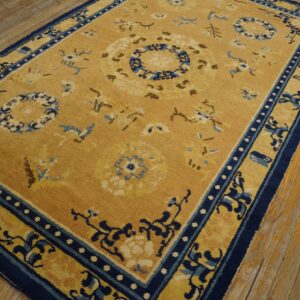 Gold rug with blue and cream floral medallions and navy borders rests on worn wood flooring.