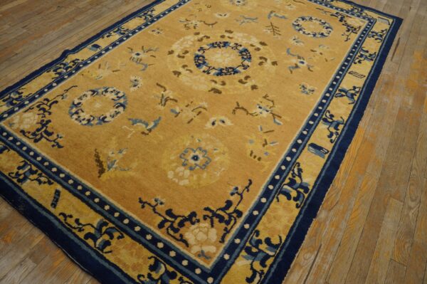 Gold rug with blue and cream floral medallions and navy borders rests on worn wood flooring.