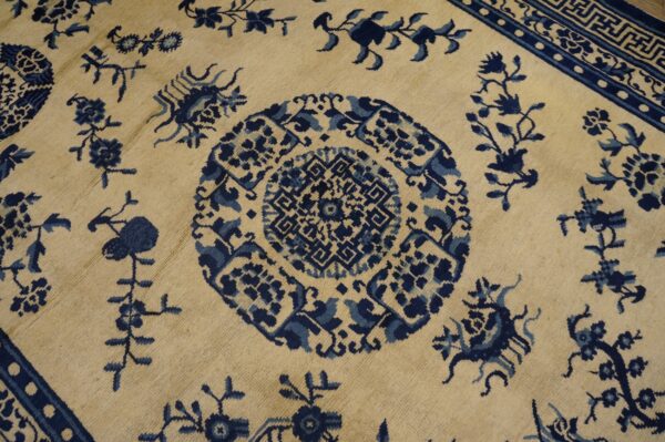 Cream rug featuring a detailed blue medallion, stylized vines, and a blue key pattern border.