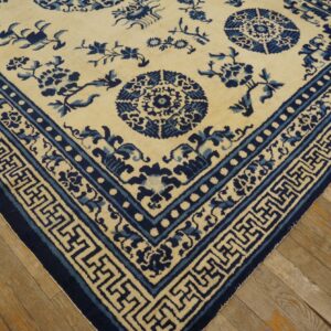 Cream rug with dark and medium blue floral patterns and geometric borders on light wood flooring.