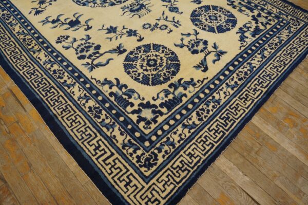 Cream rug with dark and medium blue floral patterns and geometric borders on light wood flooring.
