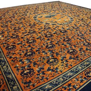 Orange rug with dark blue floral patterns and a central medallion is shown at an angle.