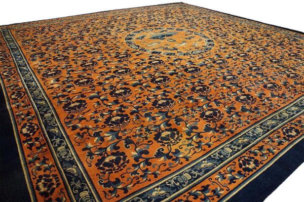 Orange rug with dark blue floral patterns and a central medallion is shown at an angle.
