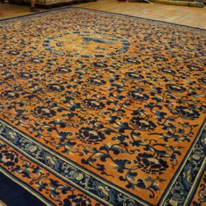 Large orange rug with dark blue floral vines and a central medallion on a wood floor.
