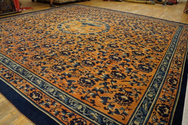 Large orange rug with dark blue floral vines and a central medallion on a wood floor.