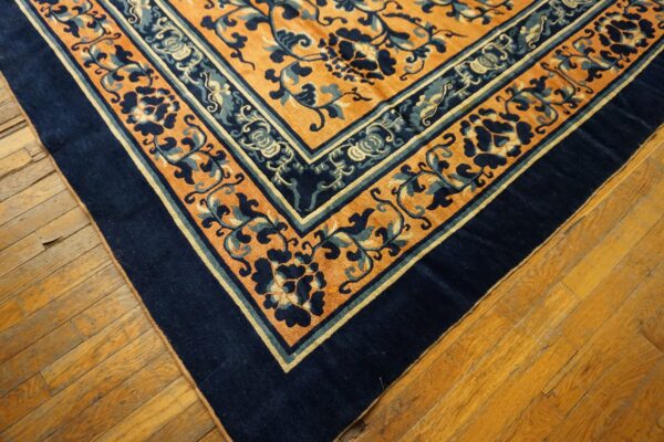 A navy and orange rug with stylized vine patterns rests on distressed golden hardwood planks.