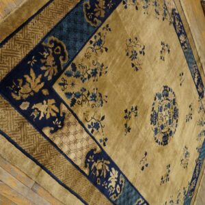 Gold and navy floral rug with complex borders sits on worn, natural wood plank flooring.