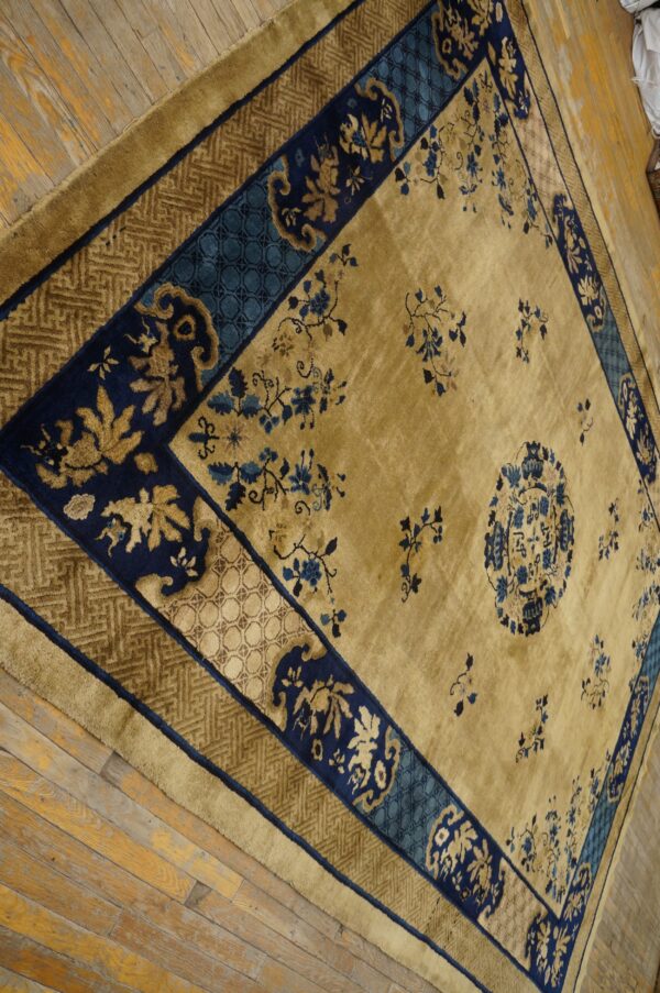 Gold and navy floral rug with complex borders sits on worn, natural wood plank flooring.