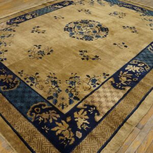 A gold and blue patterned rug with multiple borders rests on worn, diagonally oriented wooden flooring.