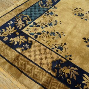 Gold high-pile rug detail showing navy blue borders, key patterns, and sparse blue floral designs on wood.